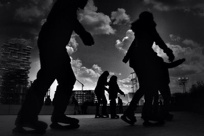 Silhouette of friends standing against cloudy sky