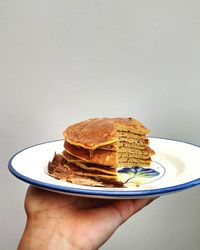 Hand holding stack of pancakes against wall