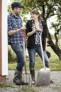 Full length of couple with pitchfork and shovel on farm