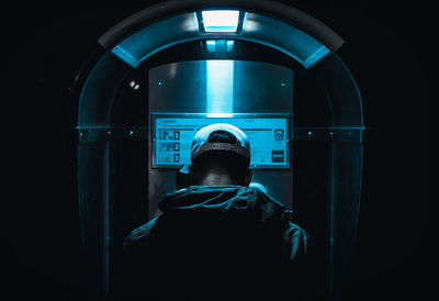 Rear view of man using pay phone at night