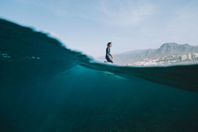 Pulled back split image of female surfer in wetsuit on a wave