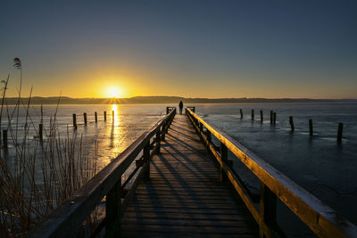 Wooden pier over sea against sky during sunset