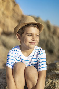 Cute boy wearing hat sitting on rock