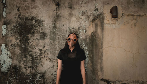 Portrait of woman wearing halloween mask standing against wall