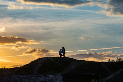 Man and woman standing on mountain against sky during sunset