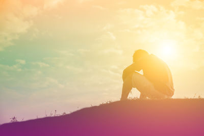 Silhouette man sitting on field against sky during sunset