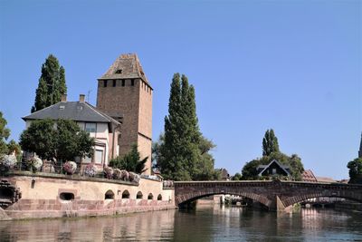 Bridge over river by buildings against clear sky