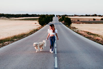 Full length of woman walking with dog on road