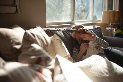 Girl hugging and kissing her dog on couch at home in pretty light