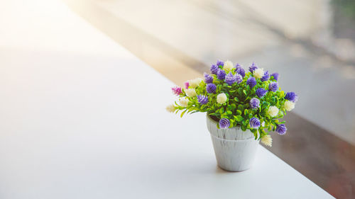 An artificial globe amaranth flower in vase on table with house and green tree blurred background