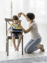 Mother cuts her son's hair by herself. little boy sits with digital tablet. new normal