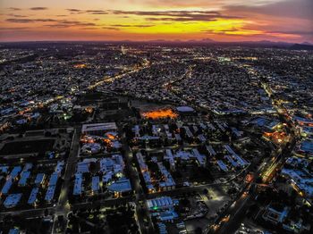 High angle view of illuminated city buildings against sky during sunset