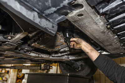 The car mechanic unscrews the diesel oil filter located in the oil pan, you can see the old oil.