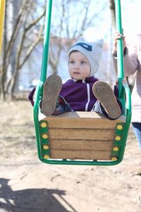 Midsection of mother standing by cute daughter swinging at playground during winter