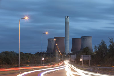 Uk, england, rugeley, vehicle light trails stretching along illuminated road at dusk with cooling towers in background