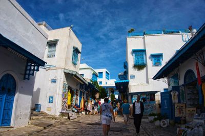 People walking on street amidst buildings in city against sky