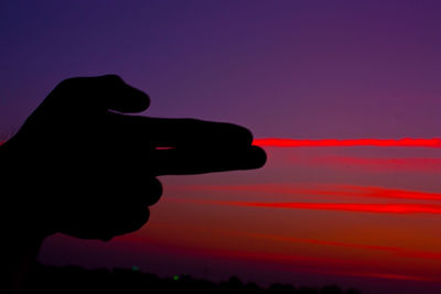 Close-up of silhouette hand gesturing gun sign against red sky during sunset