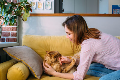 Young woman playing at home with her maine coon cat on the couch