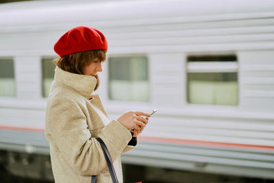 Side view of woman using phone while standing at railroad station