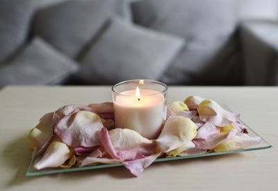 Burning candle in rose petals in the living room with a gray sofa	