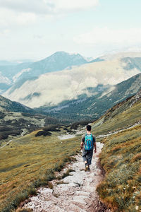 Young man with backpack hiking in a mountains, actively spending summer vacation