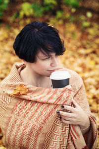 Woman holding coffee cup while standing in park during autumn
