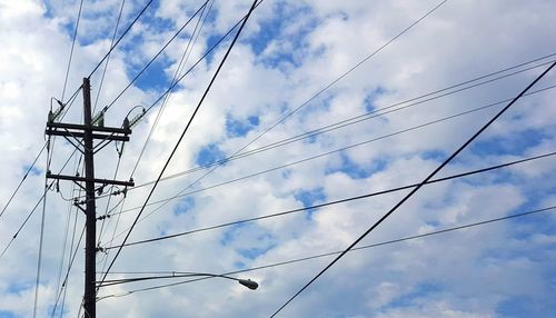 Low angle view of electricity pylon against cloudy sky