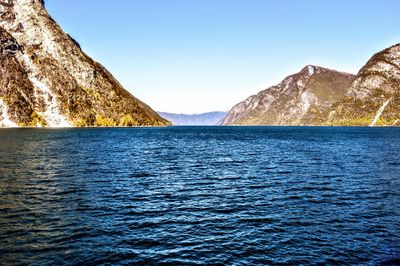 Scenic view of sea and mountains against clear blue sky