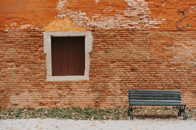 Empty bench against brick wall of old building