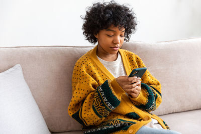 Young woman using mobile phone while sitting on sofa at home