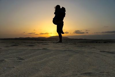 Silhouette couple standing on beach against sky during sunset