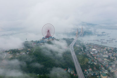 Aerial view of ferris wheel and bridge in city during foggy weather