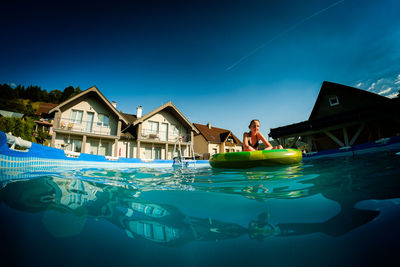 Girl with inflatable ring floating on wading pool at tourist resort against blue sky