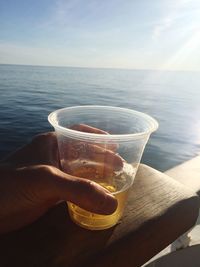 Close-up of hand holding drink in sea against sky