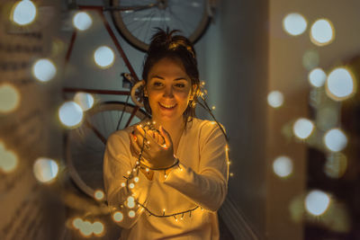 Smiling young woman holding illuminated string lights