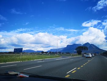 Vehicles on road against cloudy sky