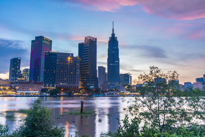 Modern buildings by river against sky in city