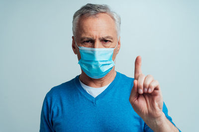 Portrait of man wearing mask gesturing against blue background