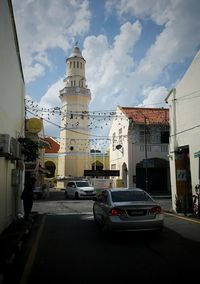 Cars on street by buildings against sky in city