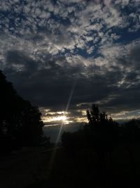 Sunlight streaming through silhouette trees against sky at sunset