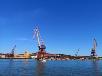 Cranes at harbor against clear blue sky