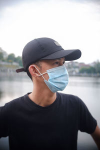 Portrait of young man wearing hat standing by lake
