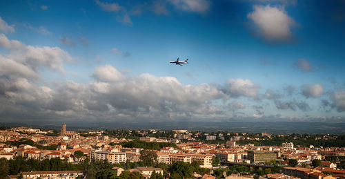 Airplane flying over cityscape against sky