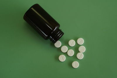 Close-up of pills spilling from bottle against green background