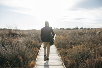 Rear view of mid adult man walking on boardwalk against sky