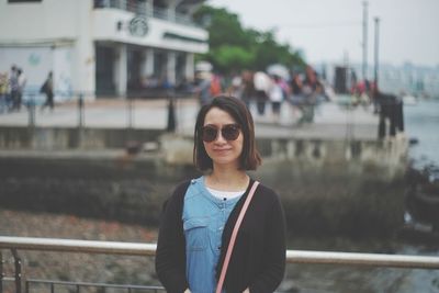 Portrait of smiling woman standing by railing in city