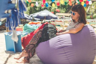 Smiling young woman wearing sunglasses while sitting on bean bag at beach
