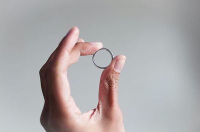Cropped image of hand holding ring over white background
