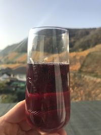 Close-up of hand holding wineglass against sky