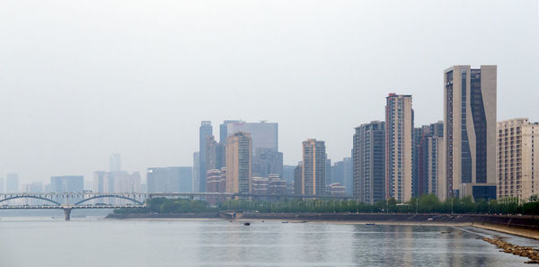 Modern buildings by river against clear sky